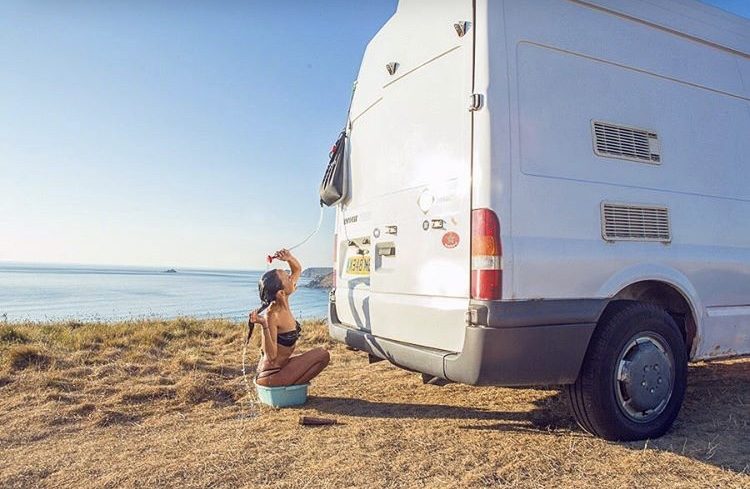 How to live off the grid- woman showering outside next to sprinter van. 