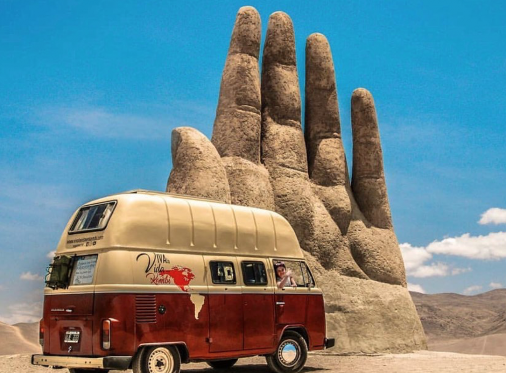 VW Bus next to a big hand carved from rock