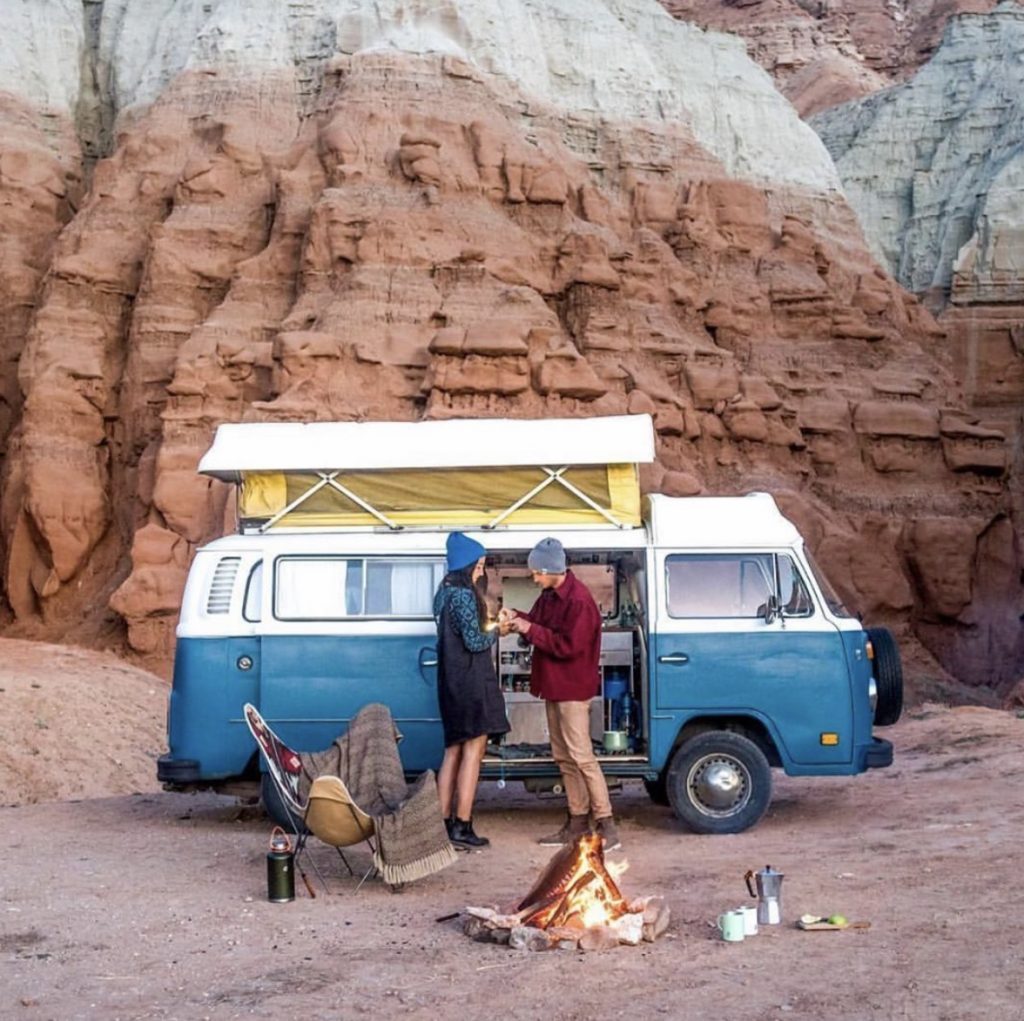 A couple out side their VW pop top in the desert. 