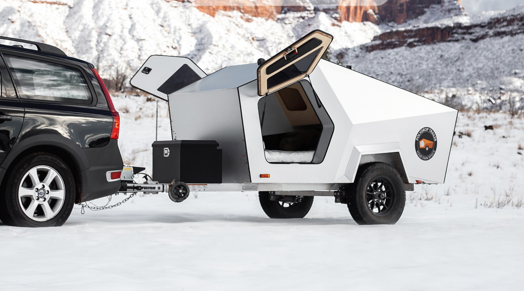 Best teardrop campers - The Polydrop Trailer being pulled by a standard saloon car. Its Delorian style doors are open, and this camper utilises lots of straight lines and geometric design elements