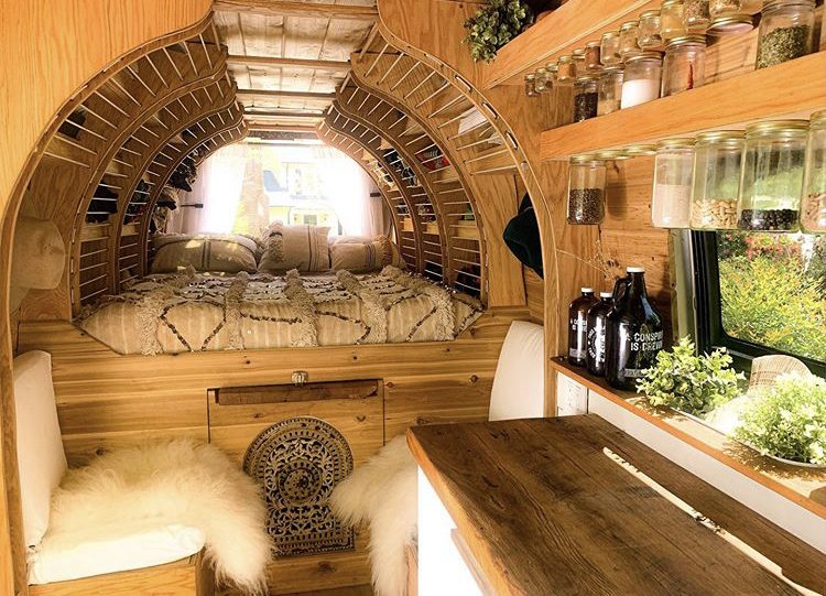 Wooden van interior with curved shelving around fixed double bed at back. 