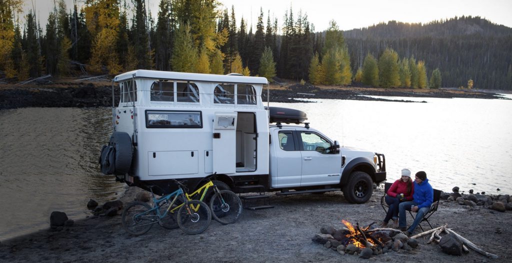 Best RVs- EarthCruiser EXD exterior with roof popped, infront of lake with campfire and people sat around 