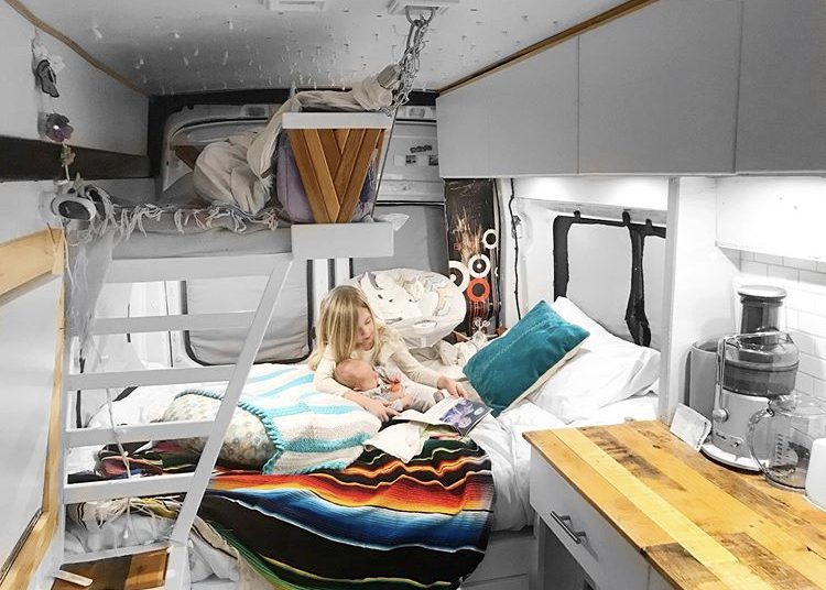 Custom van ideas - inside of bed with static bed at back and bunk bed above for kid. Kid holing baby on bed reading books. 