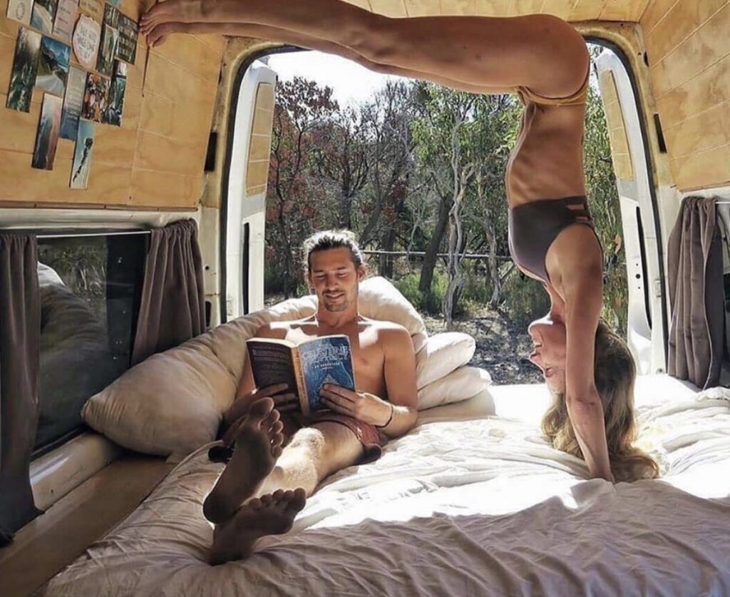 Woman doing yoga and man reading on bed in campervan 