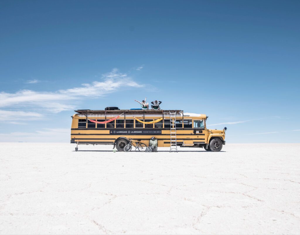 School bus camper - skoolie on salt planes with two people sat on top 