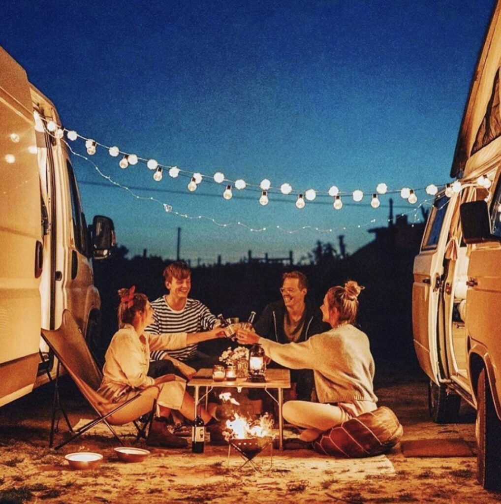 four people sat sharing drinks between two camper vans 
