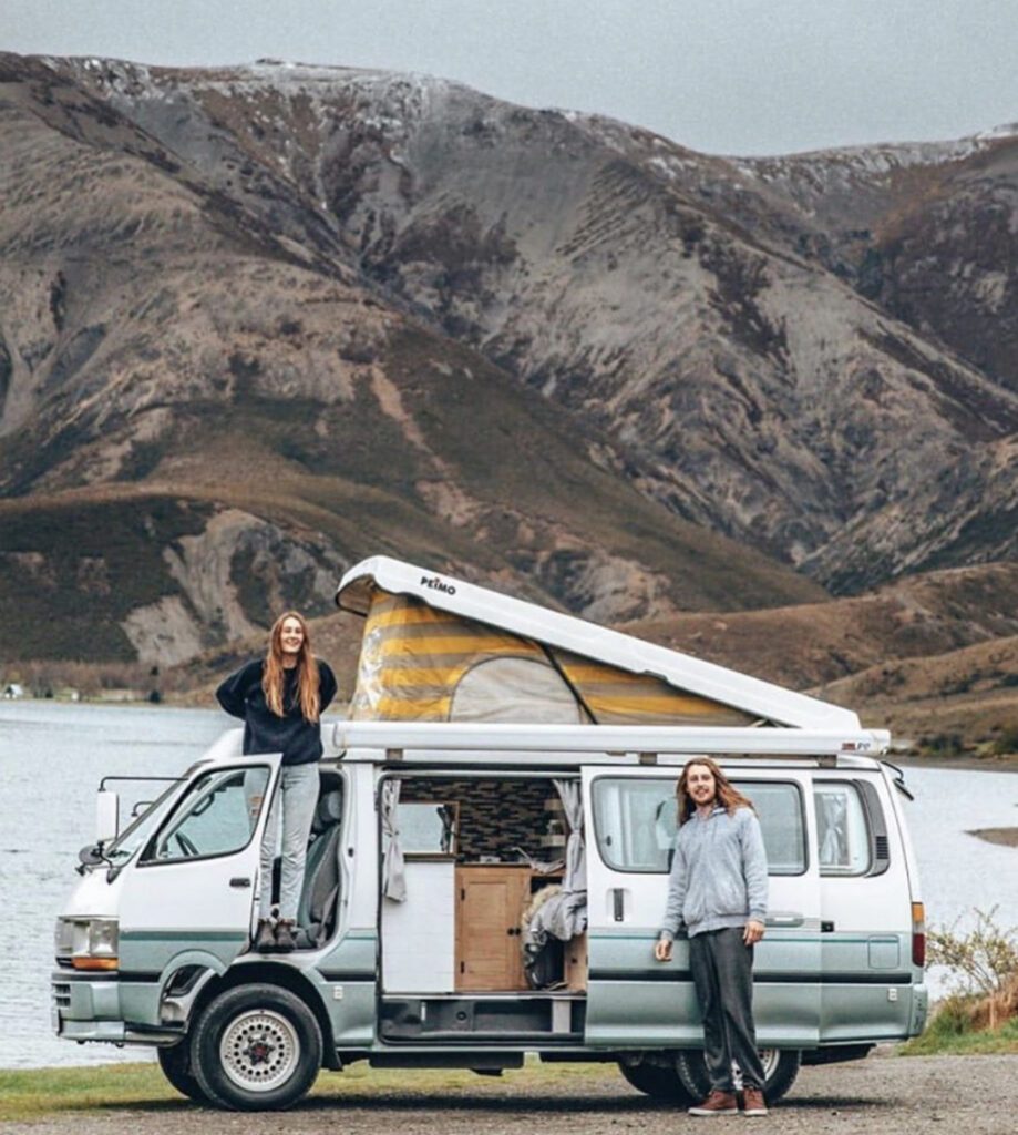 Pop top camper with roof up infront of lake and mountains 